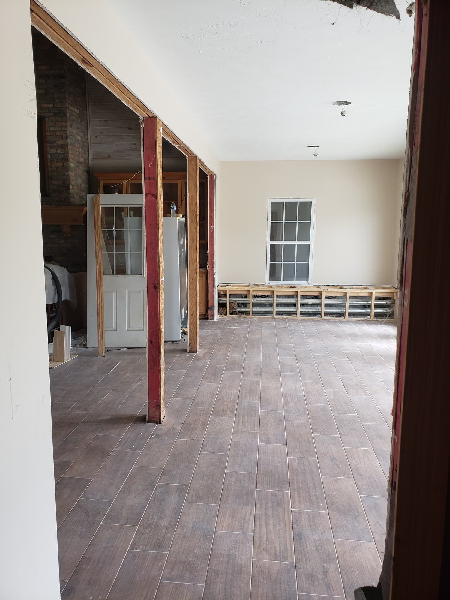 A newly framed structural header spanning a widened opening above a wood-look porcelain tile floor