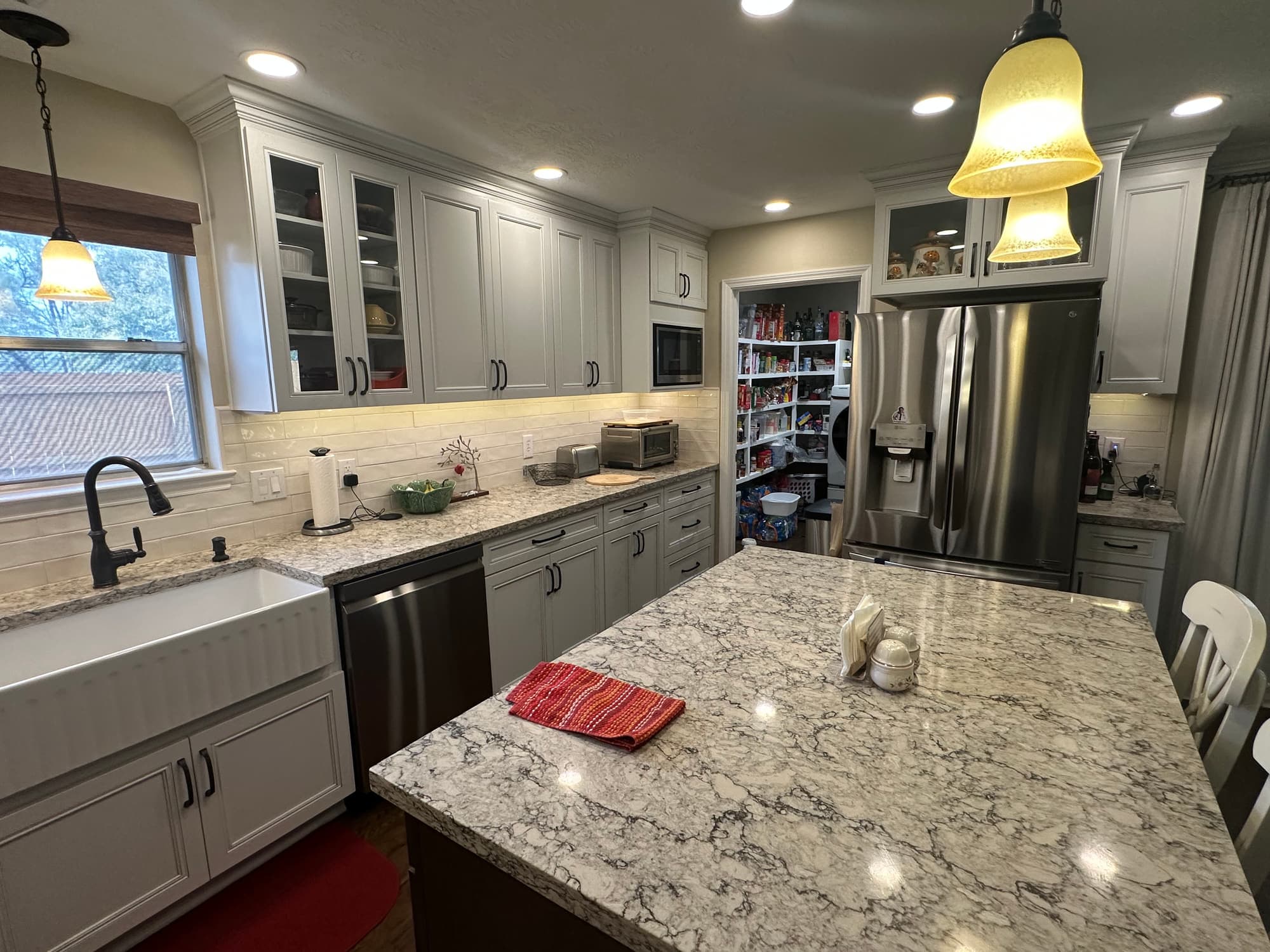 Finished kitchen remodel with a quartz-topped island, painted shaker cabinets, a farmhouse apron sink and a cream subway tile backsplash