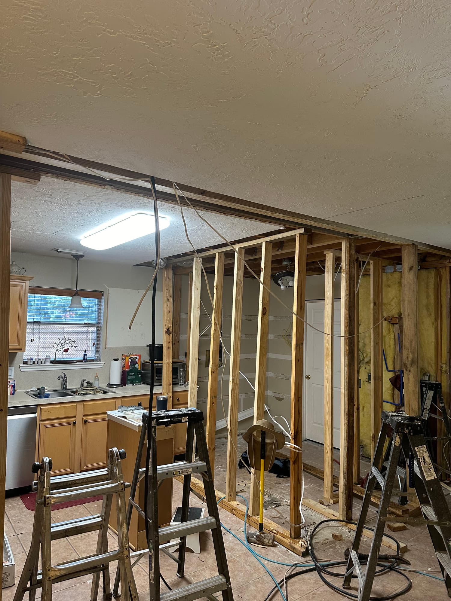 Ceiling framing exposed down to the joists during a remodel, with new lumber, wiring runs and work ladders in place